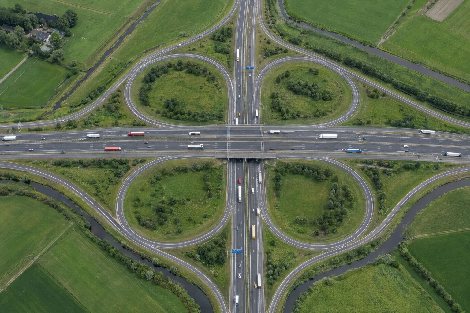 Luchtfoto van een Nederlands snelwegknooppunt met vrachtwagens tussen weilanden