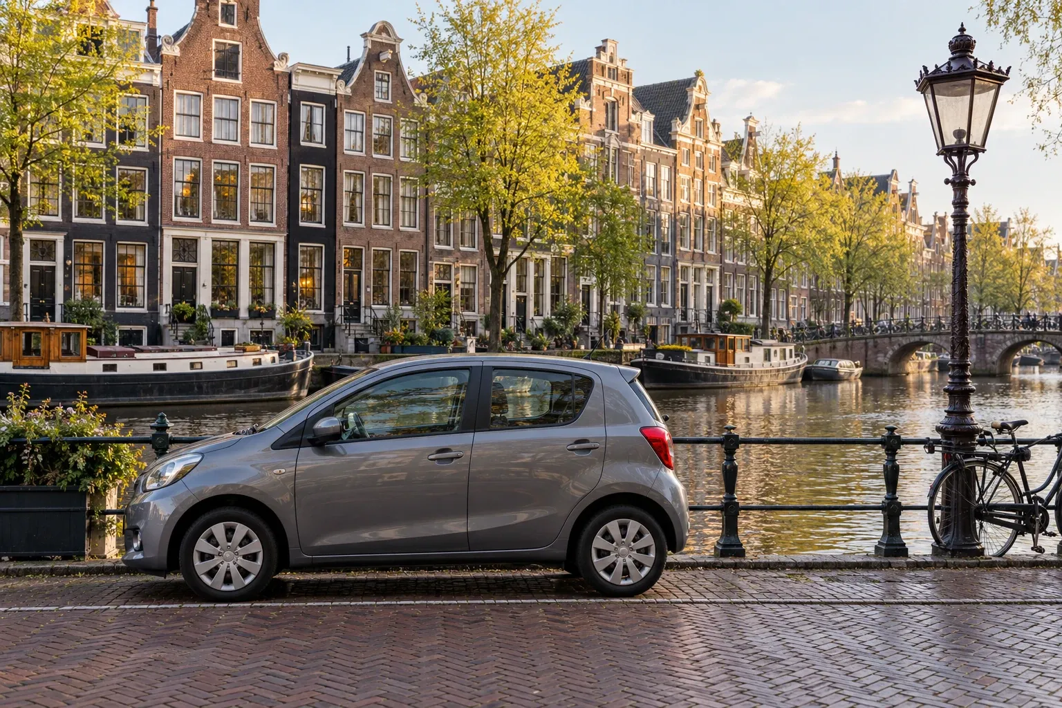 Grijze kleine auto geparkeerd langs gracht met rijksgrachtenpanden en fiets tegen railing